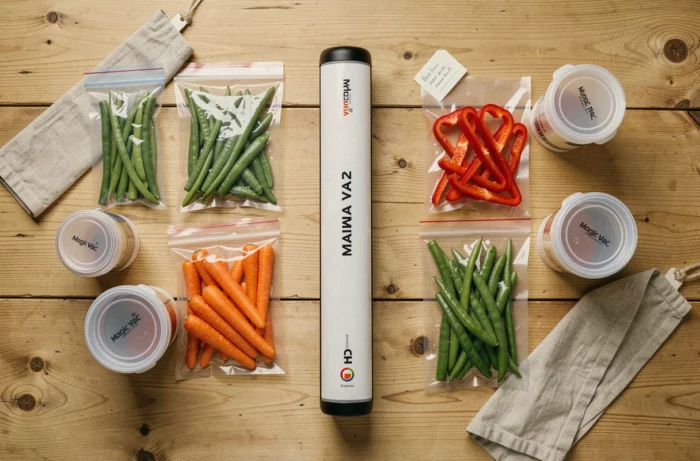 Vue de dessus de la Magic Vac Maxima 2 entourée de sachets sous vide contenant des légumes frais colorés sur une table en bois rustique